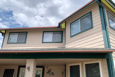 A two story house with light tan siding and green trim is shown.