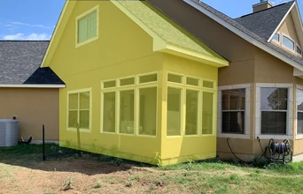 A bright yellow sunroom addition with windows highlights a home’s corner.