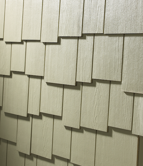A close up of beige staggered shingle siding where the thing boards are laid unevenly on the siding.
