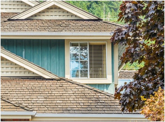 A home's blue siding, brown shingles and a window with blinds.