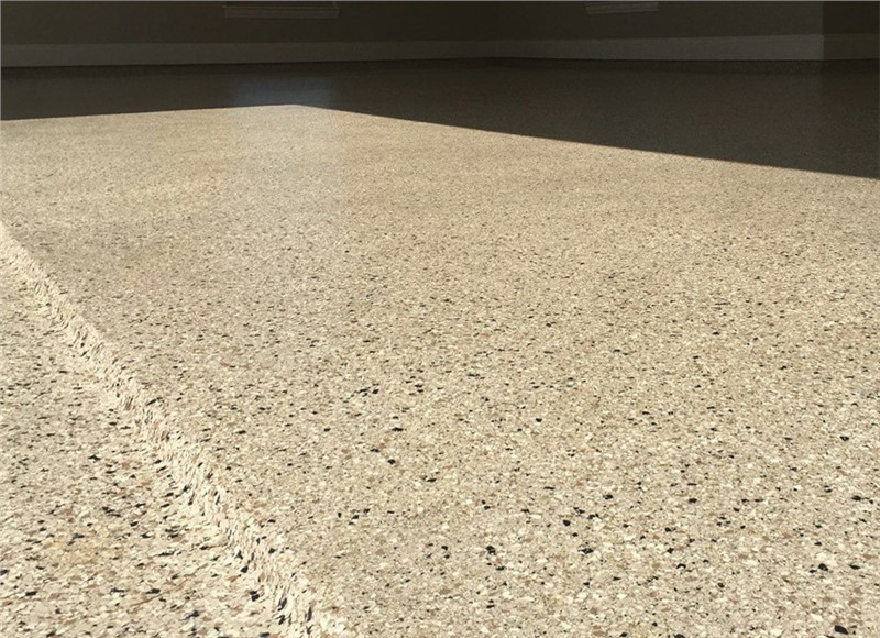 A close up of a garage floor apron and lip with a concrete coating that looks like granite with tan, white, and black vinyl chips in the coating. 