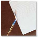 A close-up shot of a paintbrush touching the corner of a white paper on a brown surface.