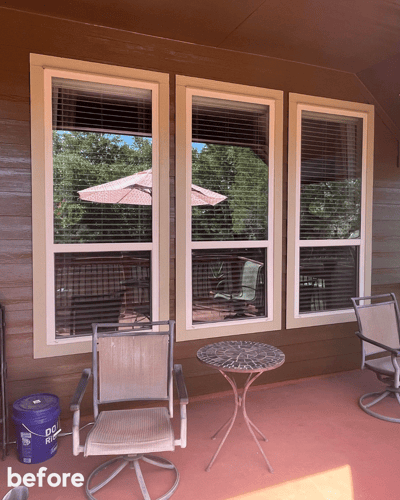 The before picture of an exterior of three white windows on a patio. 