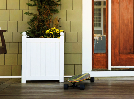 A white planter sits on a wooden porch next to a door.