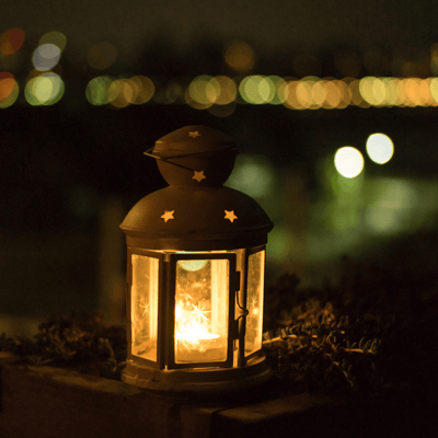 A glass lantern lit with star cutouts at the top with a dark, night time background.