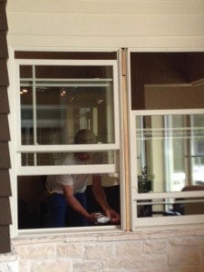 A man is shown from the waist up, working on a window frame.