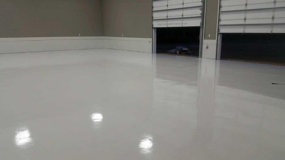 A garage floor with a shiny grey epoxy coating and the doors cracked open.