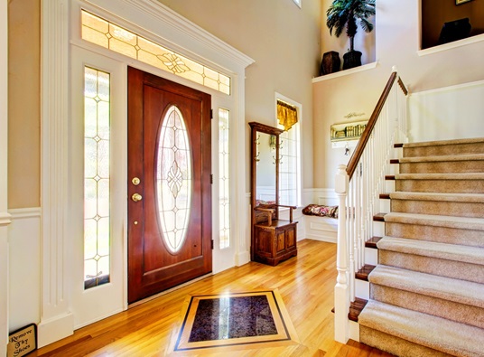 A bright entryway has a wood door, hardwood floors, and stairs.