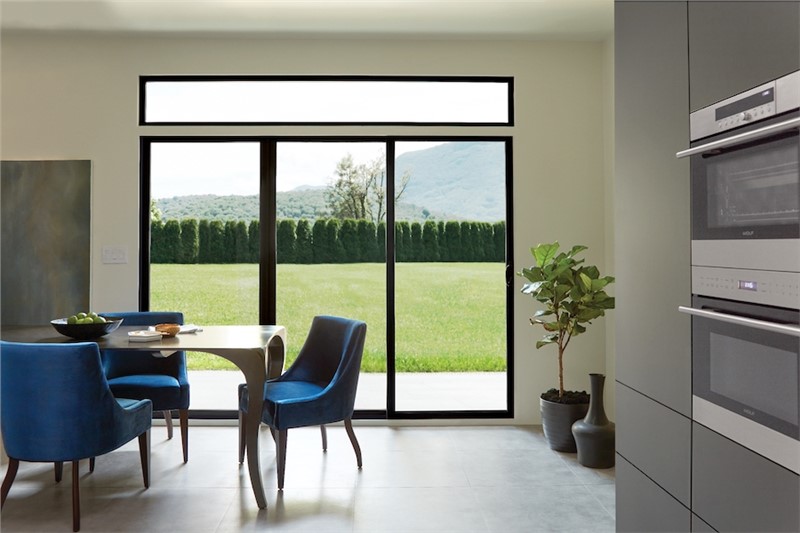 A kitchen/dining room area with blue velvet chairs at table in front of a large patio sliding door with a view of a yard.