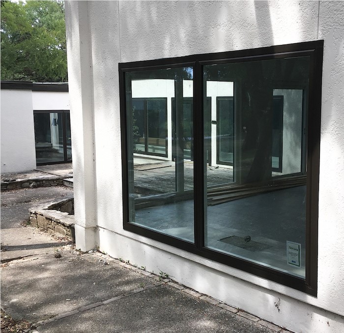 The side of a house with white stucco and a large double casement window that is black. 