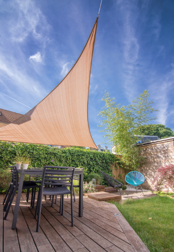 A sand colored shade sale over a patio deck with an outdoor seating area on a backyard. 