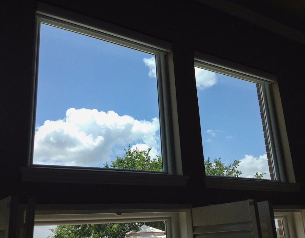 Windows at the top of a wall looking from the inside of a home. The windows are square and in a line with a blue sky and clouds behind.