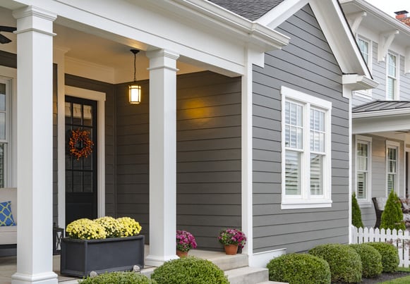 A close view of the exterior of a house with gray siding, white trim, and white columns. 