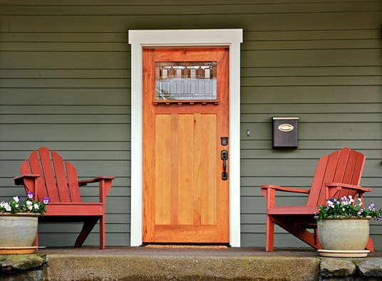 A photo of a house's front porch is shown with two red chairs, flowers, and a wood door in the center.