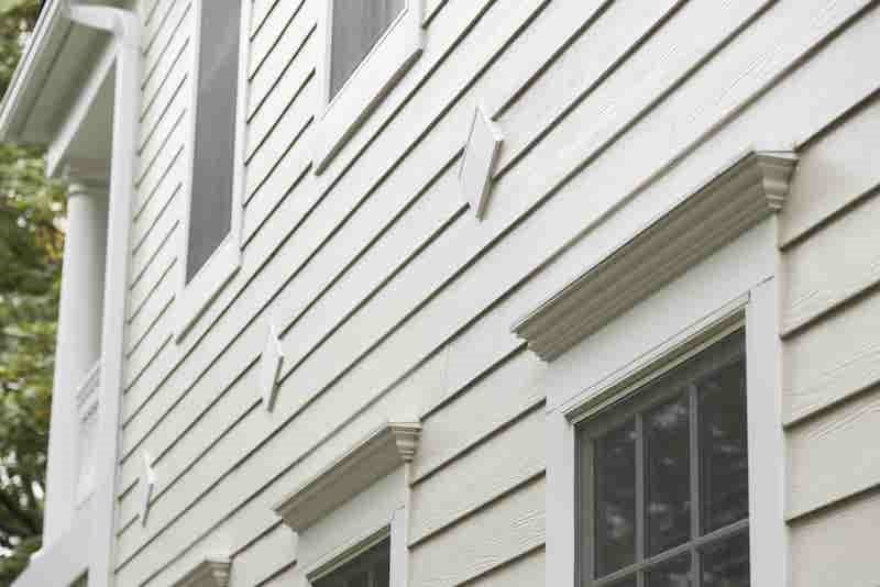 Close-up of a home's light-colored siding with decorative trim around windows.