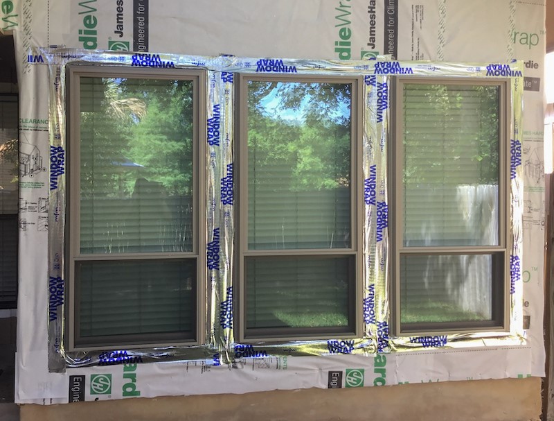 The side of a house with three windows, the walls are exposed under construction and a silver tape is around the windows.