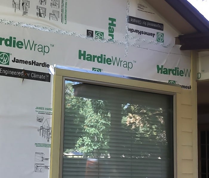 The side of a house with the siding exposed under construction and one single window. There is a silver metal strip above the window.