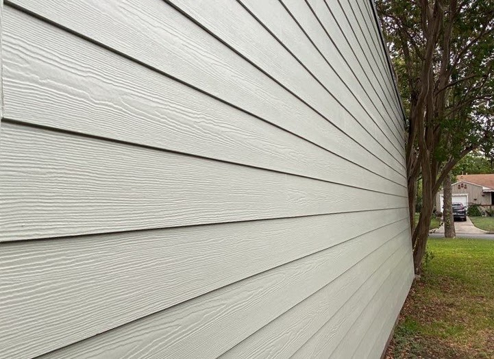 A close-up shot of light gray horizontal siding with a wood-grain texture.